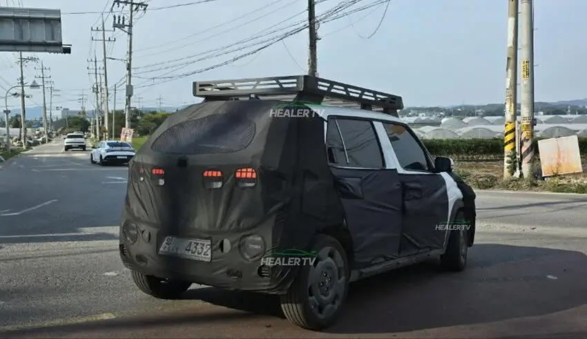 Automóvil camuflado circulando por una carretera con invernaderos a un lado.