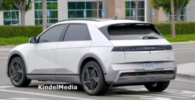 Auto blanco estacionado en calle, cerca de edificio moderno.