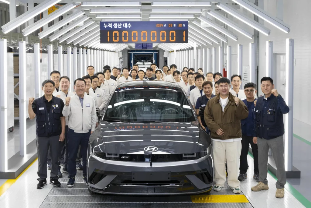 Un grupo de personas posando con un auto nuevo en una fábrica.