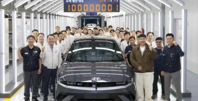 Un grupo de personas posando con un auto nuevo en una fábrica.