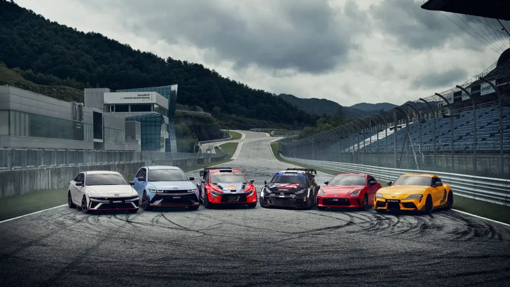 Seis coches deportivos en una pista de carreras con montañas.