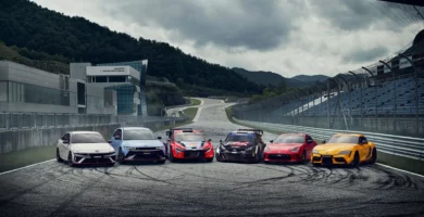 Seis coches deportivos en una pista de carreras con montañas.