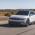 Coche blanco eléctrico en carretera desértica bajo cielo despejado.