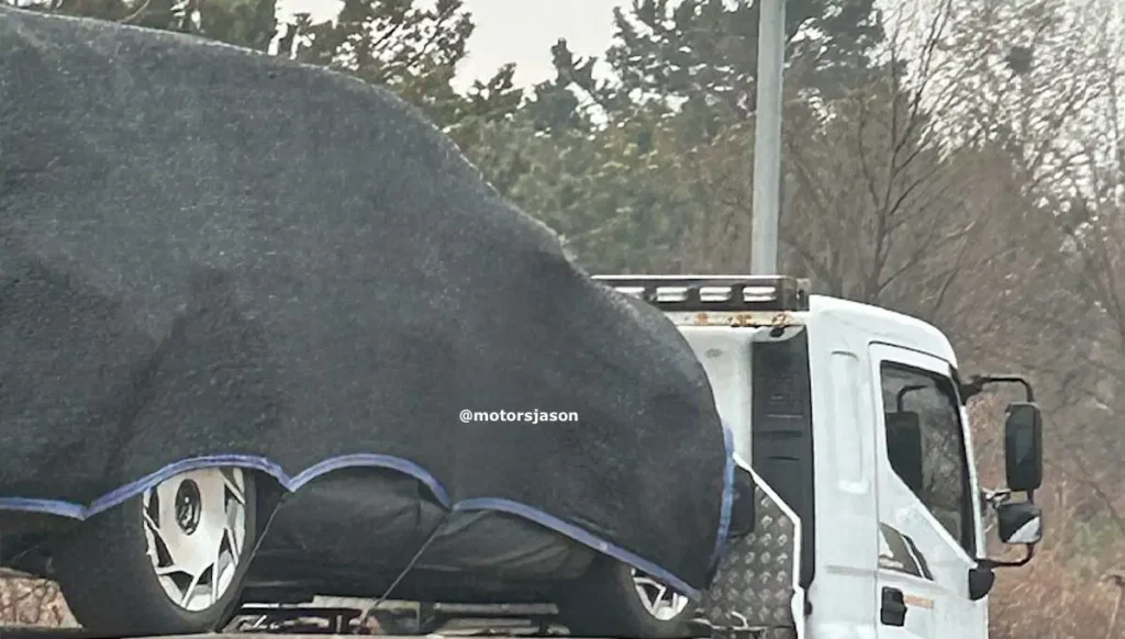 Camión transporta un vehículo cubierto por una lona negra.