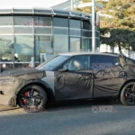 Auto camuflado en pruebas cerca de un edificio moderno.