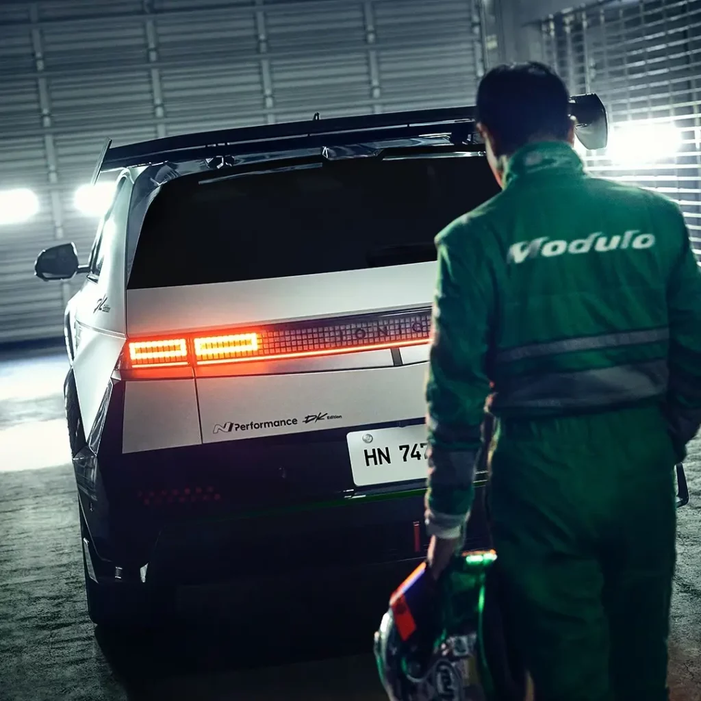 Persona con uniforme verde junto a un auto deportivo en un garaje.