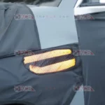 Parte de un automóvil camuflado, mostrando las luces traseras encendidas.