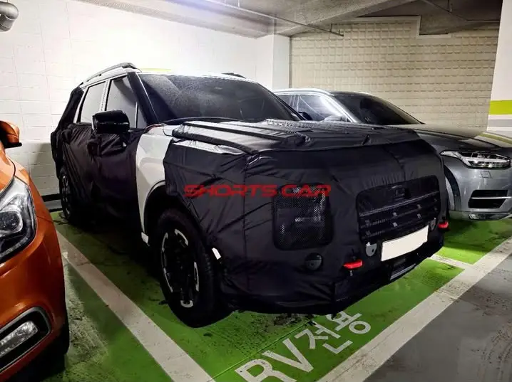 Coche cubierto con lona negra en estacionamiento subterráneo.